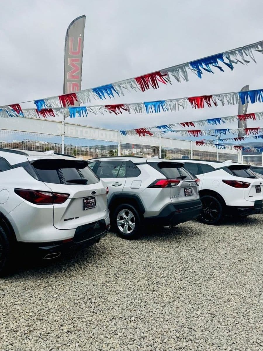 Fila de SUVs blancas en el lote de Ixchel's Automotriz, bajo banderines de colores